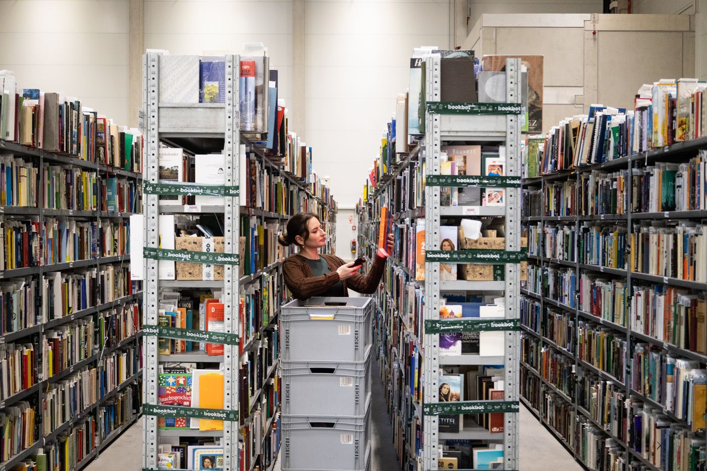 Brigádnice skenuje knihu mezi regály v logistickém centru